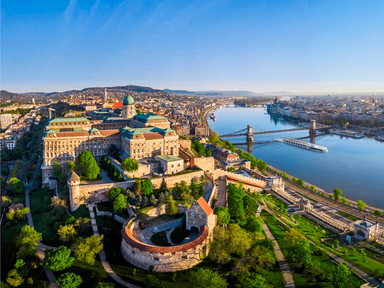Aerial view of Budapest cityscape with the Danube River flowing through it and the Scenic Jasper ship cruising along the river. 