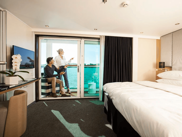 A man and woman looking out to the river from their Scenic Sun Lounge in the Junior Balcony Suite
