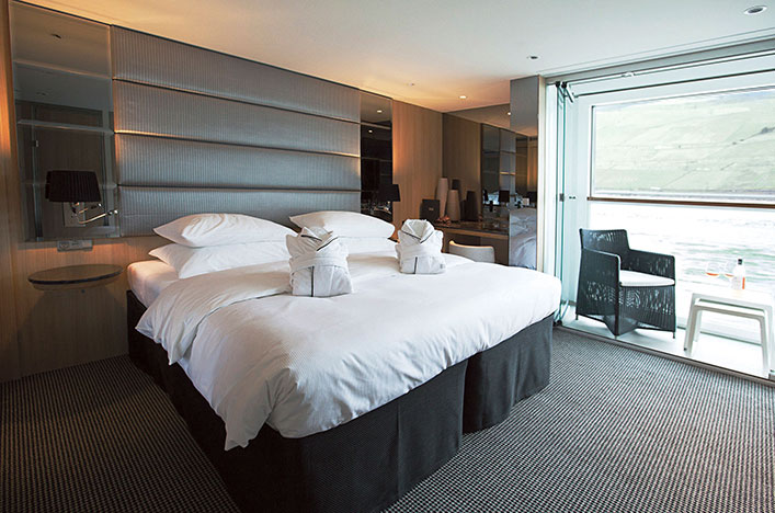 A bed situated beside a floor-to-ceiling window in the Balcony Suite, offering a view of the Douro River.
