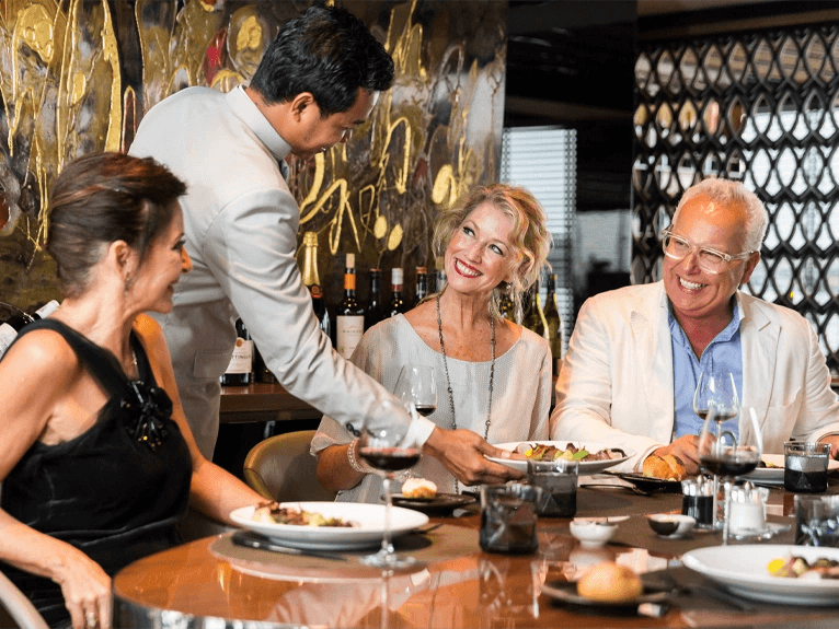 Three guests being served dinner by a waiter in the Chef’s Table Dining area on board Scenic Spirit ship