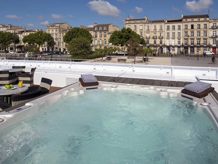 An outdoor pool located on the sunlit top deck of the Scenic Diamond cruise ship, with views of the surrounding historic buildings. 