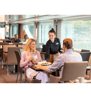 A man and woman being served plates of food by a waiter in the Crystal Dining area on board a Scenic cruise ship.