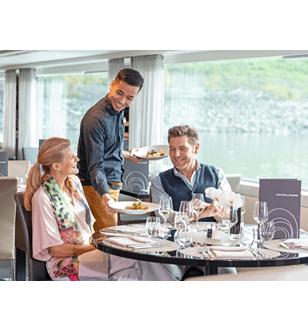 A man and woman being served food by a waiter at a table in Crystal Dining on a Scenic cruise ship.