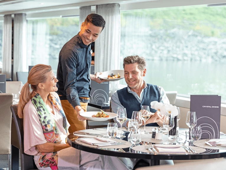  A man and woman being served food by a waiter at a table in Crystal Dining on a Scenic cruise ship.  
