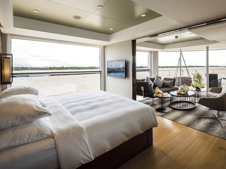 A Royal Panorama Suite with a queen bed and a separate lounge area, enhanced by floor-to-ceiling windows with views of the Mekong River.
