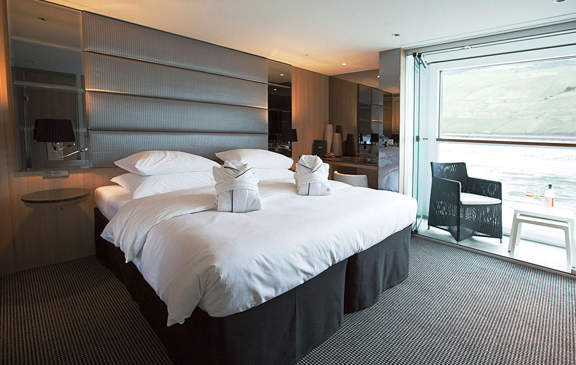 A Queen bed and the Scenic Sun Lounge area in the Deluxe Balcony Suite.