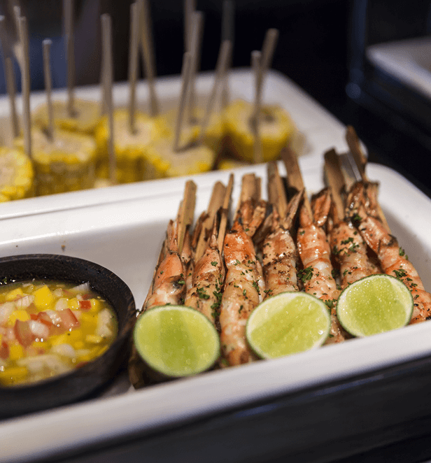 Grilled prawns served with lime wedges and mango salsa, with corn skewers in the background.