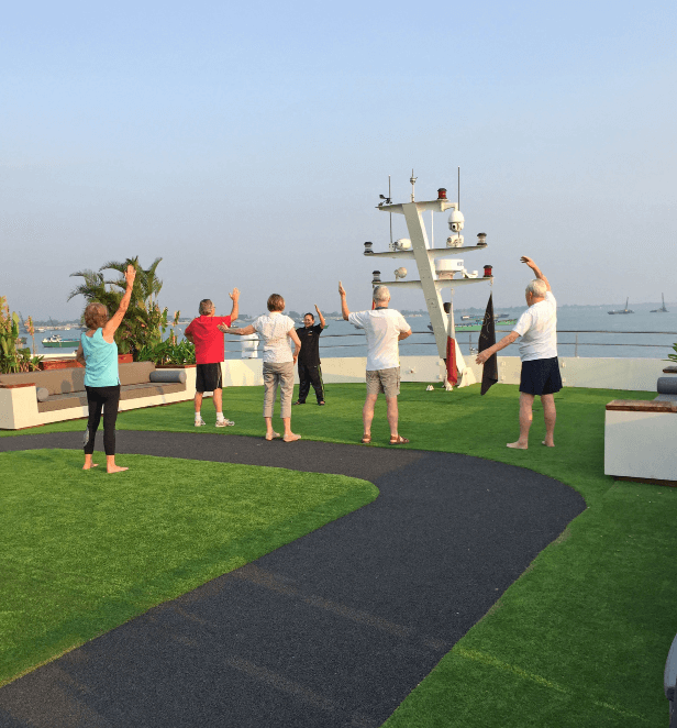 Group of guests participating in a morning tai chi class on the sun deck of a Scenic river cruise ship with ocean views.