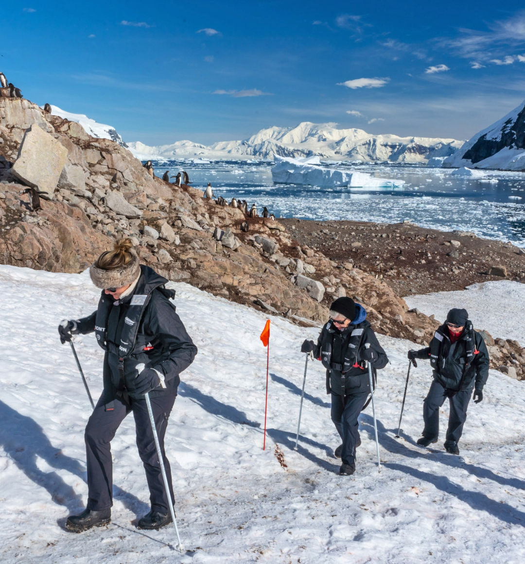 Walkers hiking up snow covered hillside with polar scenery behind