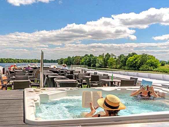 Two guests relax reading books in the vitality pool on the Sun Deck as other guests sit in the background 