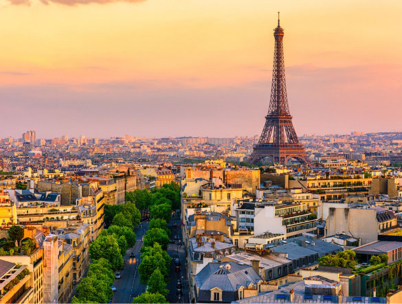 Wide shot of the Eiffel Tower and the city of Paris with a tree-lined street and a pastel-coloured sunset in the background