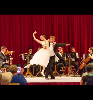 Ballet dancers perform at an exclusive concert with an orchestra and red curtains behind